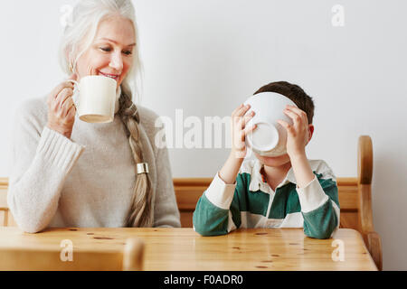 Boy drinking milk from bowl with grandmother Stock Photo