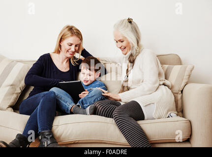 Young boy using digital tablet with mother and grandmother Stock Photo