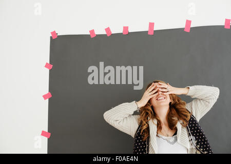Mid adult woman smiling, hands covering eyes Stock Photo