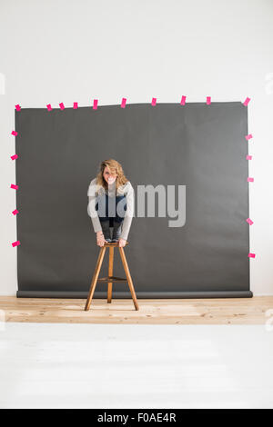 Mid adult woman crouching on top of stool Stock Photo