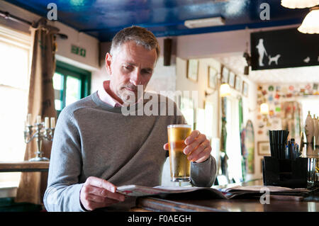 Mature man drinking beer and reading newspaper in pub Stock Photo