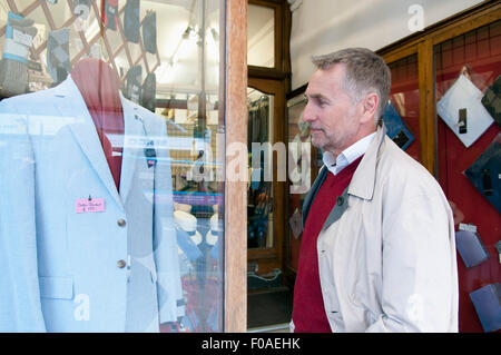 Mature man looking at suit jacket in tailors shop window Stock Photo