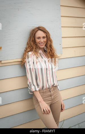 Attractive redhead woman smiling leaning against beach hut Stock Photo