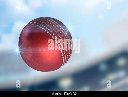 A regular red cricket ball flying through the air on a stadium background during the daytime Stock Photo