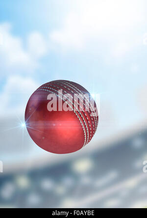 A regular red cricket ball flying through the air on a stadium background during the daytime Stock Photo