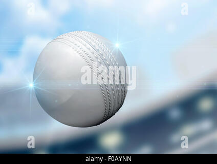 A regular white cricket ball flying through the air on a stadium background during the daytime Stock Photo