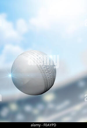 A regular white cricket ball flying through the air on a stadium background during the daytime Stock Photo