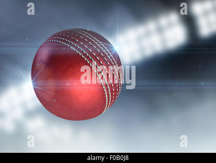 A regular red cricket ball flying through the air on an indoor stadium background during the night Stock Photo