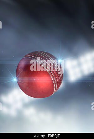 A regular red cricket ball flying through the air on an indoor stadium background during the night Stock Photo