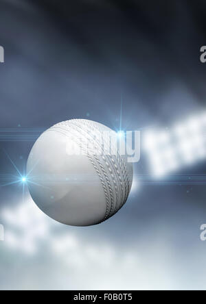 A regular white cricket ball flying through the air on an indoor stadium background during the night Stock Photo