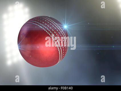 A regular red cricket ball flying through the air on an a outdoor stadium background during the night Stock Photo