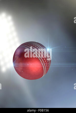 A regular red cricket ball flying through the air on an a outdoor stadium background during the night Stock Photo