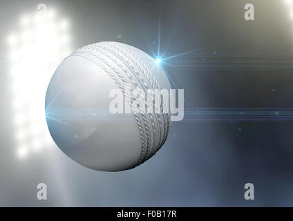 A regular white cricket ball flying through the air on an a outdoor stadium background during the night Stock Photo