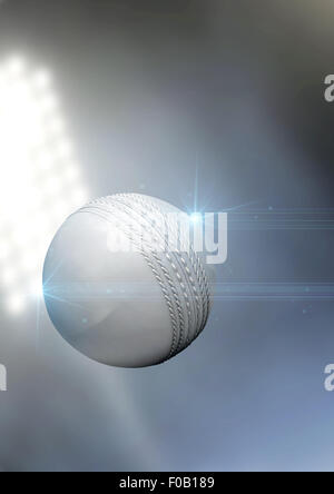 A regular white cricket ball flying through the air on an a outdoor stadium background during the night Stock Photo