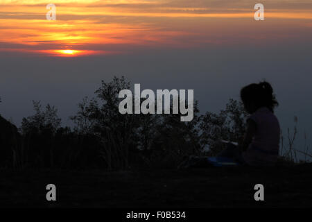 Silhouette of a little girl painting picture of sunset on a hill top - shot from Ponmudi, a tourist attraction of Kerala, India Stock Photo