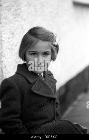 A young girl in her coat sitting outside a house Stock Photo