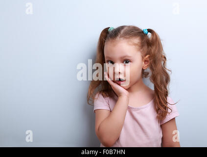 Cute funny kid girl surprising with open mouth on blue background Stock Photo