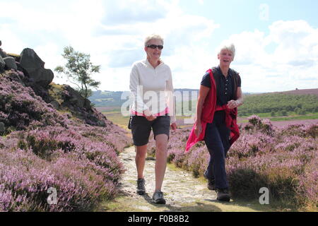 Walkers pass flowering heather on Burbage Edge near Sheffield  in the Peak District National Park, England UK Stock Photo