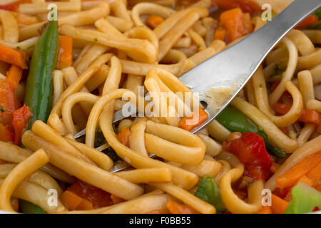 Close view of sesame seasoned noodles with assorted vegetables with a fork inserted in the food illuminated with window light. Stock Photo