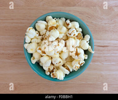 Top view of a small bowl filled with a serving of white cheddar cheese flavored popcorn on a wood table top Stock Photo