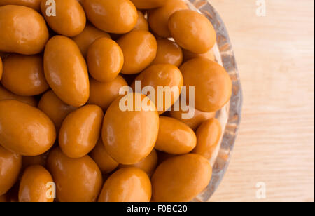 Top close view of a glass bowl filled with caramel coated raisins on a wood table illuminated with natural light. Stock Photo