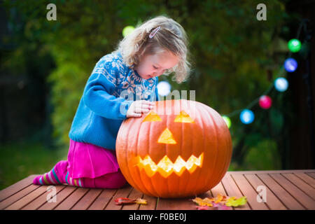 Little girl carving pumpkin at Halloween. Dressed up child trick or treating. Kids trick or treat. Child in witch costume Stock Photo