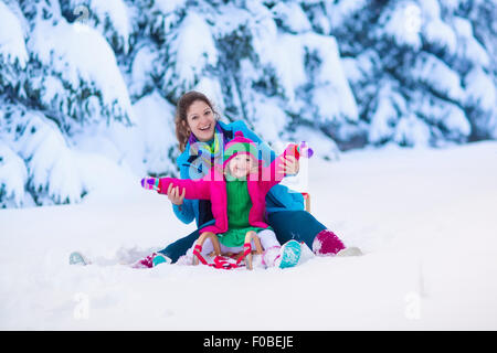 Young mother and little girl enjoying sleigh ride. Child sledding. Toddler kid riding sledge. Children play outdoors in snow. Stock Photo