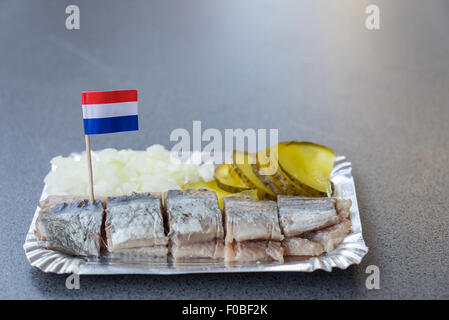 A Dutch herring cut up into slices and served with sliced gherkin and onion. Stock Photo