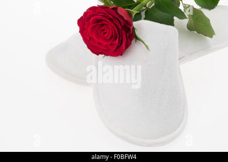 A red rose and a white pair of hotel or spa slippers - studio shot with a white background Stock Photo