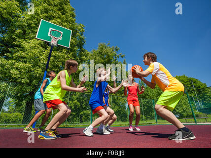 Teenage children playing basketball game together Stock Photo