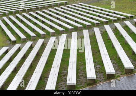 Rows of wooden benches on hillside of outdoor concert area, wet seats after rain Stock Photo