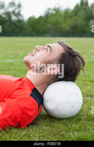 Side view of young man resting head on soccer ball in field Stock Photo