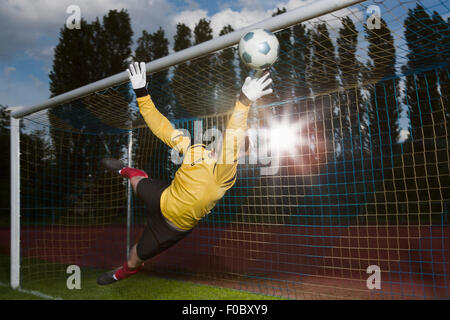 Full length of soccer goalkeeper diving to block ball Stock Photo