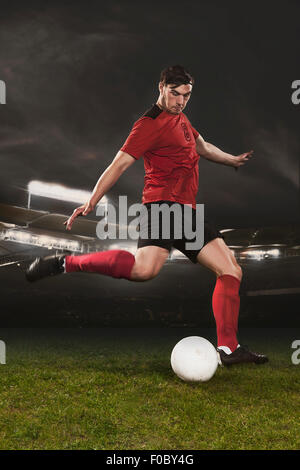 Full length of young soccer player kicking ball on field Stock Photo