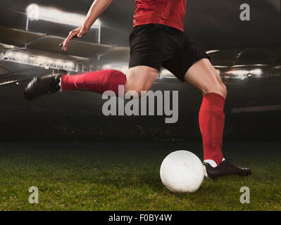 Low section of young soccer player kicking ball on field Stock Photo