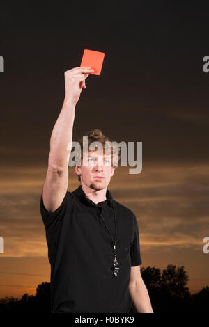 Young soccer referee holding up red card during sunset Stock Photo