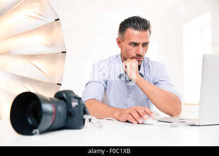 Portrait of a handsome photographer using laptop at his workplace Stock Photo