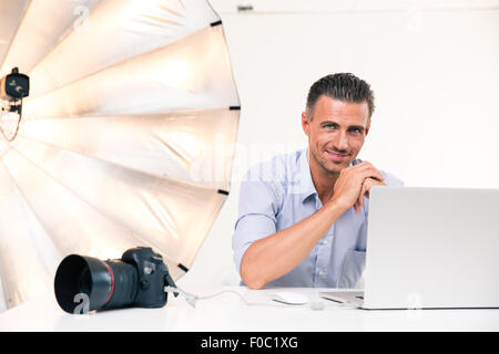 Portrait of a smiling photographer using laptop at his workplace and looking at camera Stock Photo