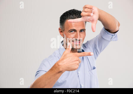 Portrait of a smiling businessman making frame with fingers and looking at camera over gray background Stock Photo
