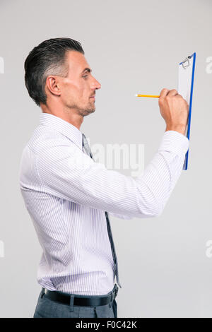 Side view portrait of a businessman writing notes in clipboard isolated on aw hite background Stock Photo