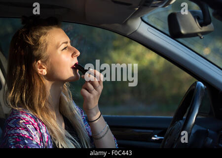 brunette woman putting on some lipstick in her car Stock Photo