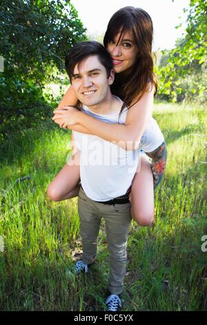 Young man giving girlfriend piggyback ride in park