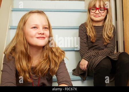 Two sisters sitting on stairs, smiling Stock Photo