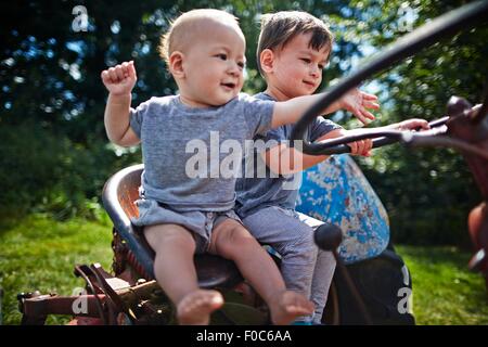 Baby boy and boy playing on old tractor Stock Photo