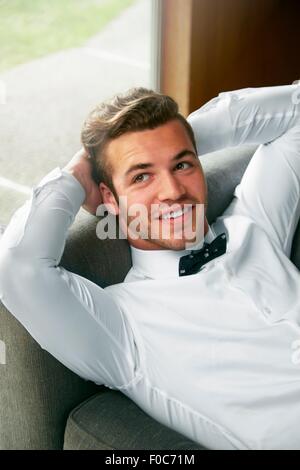 Portrait of man wearing bow tie reclining on sofa with hands behind head Stock Photo
