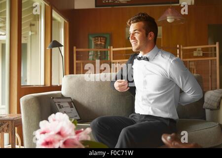 Man in smart clothes sitting on sofa putting on jacket Stock Photo