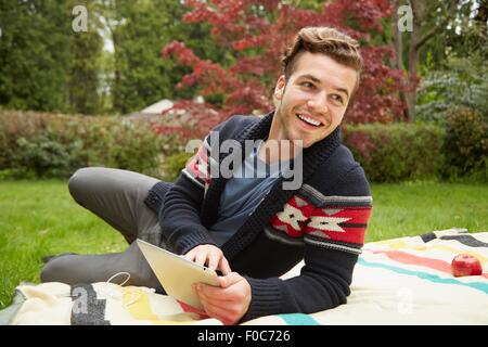 Portrait of smiling man laying in garden reading digital tablet Stock Photo