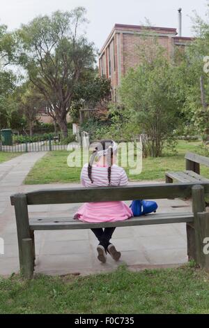 Young girl sitting on bench, rear view Stock Photo