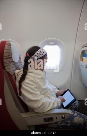 Young girl sitting in seat on aeroplane using digital tablet Stock Photo