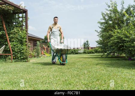 Young man walking with wheelbarrow in backyard Stock Photo